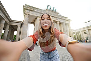 Travel in Berlin. Happy tourist woman takes selfie picture with smartphone camera in front of Brandenburg Gate, Berlin, Germany.