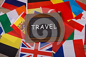 Travel - blackboard with text "Travel", flags of different countries on wooden background