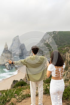 Travel blog concept. Lady making photo on cellphone of european man standing back to her, coastline view, vertical shot
