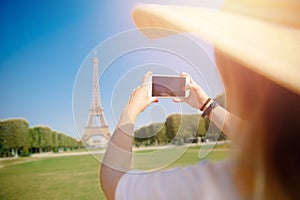 Travel blogger young woman in hat takes photograph of Eiffel Tower on telephone in Paris, France