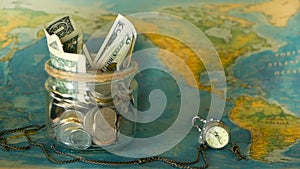 Travel budget concept. Money saved for vacation in glass jar on world map background