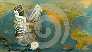 Travel budget concept. Money saved for vacation in glass jar on world map background