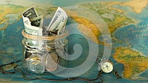 Travel budget concept. Money saved for vacation in glass jar on world map background