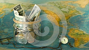 Travel budget concept. Money saved for vacation in glass jar on world map background