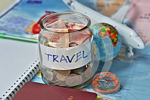 Travel budget concept. travel money savings in a glass jar with compass, passport and aircraft toy