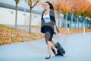 Travel. Business Woman in airport talking on the smartphone while walking with hand luggage in airport going to gate