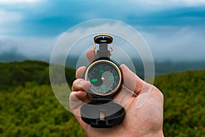 Travel, camping, orienteering and navigation concept - black magnetic compass close-up in a man s hand, blurred landscape