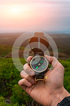 Travel, camping, orienteering and navigation concept - black magnetic compass close-up in a man s hand, blurred landscape