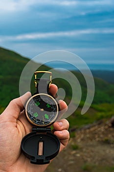 Travel, camping, orienteering and navigation concept - black magnetic compass close-up in a man s hand, blurred landscape