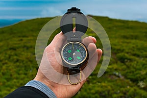 Travel, camping, orienteering and navigation concept - black magnetic compass close-up in a man s hand, blurred landscape