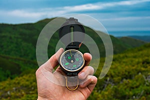 Travel, camping, orienteering and navigation concept - black magnetic compass close-up in a man s hand, blurred landscape