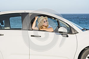 Travel by car. Cheerful happy woman looking outside the white vehicle in sea view parking. Concept of summer renting transport and