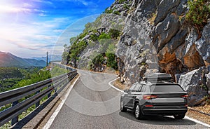 Travel car drives along the highway against the backdrop of mountains on a sunny day.