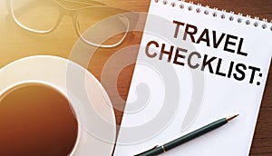 TRAVEL CHECKLIST - text on paper with cup of coffee and glasses on wooden background in sinlight