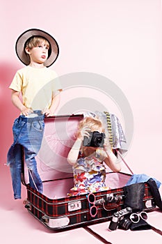 Travel: Children little boy and girl pack things in a big red suitcase for travel. The child holds in his hands a large camera