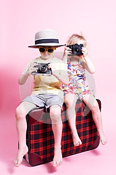 Travel: Children a little boy and girl play in tourists, sit on a big red suitcase and take pictures