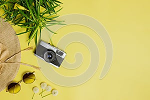 Travel concept with camera, green leaves, sun glasses and hat over the yellow background.