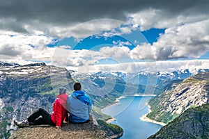 Travel concept. The couple sitting on a cliff over a lake, Trolltunga, Norway. Amazing nature view. Artistic picture. Beauty world