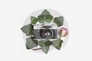 Travel concept - floral frame made of green ivy leaves, nymphaea waterlily purple flowers and vintage retro camera in the middle