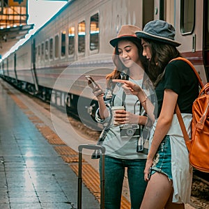 Travel concept. grils friend wear hat holding smartphone have bag and luggage.female traveller at train station with train