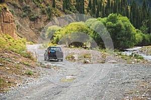 Travel concept with little green 4x4 off-road car driving in summer mountains mud road