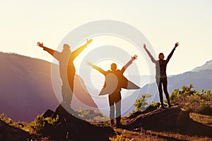 Travel concept with three happy friends against sunset mountains