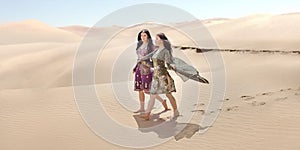 Travel concept. Two gordeous women sisters traveling in desert. Arabian Indian movie stars.