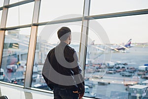 Travel concept with young man in airport interior with city view and a plane flying by.