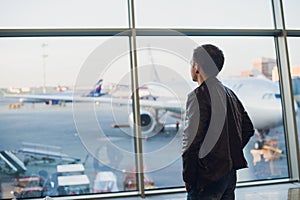 Travel concept with young man in airport interior with city view and a plane flying by.