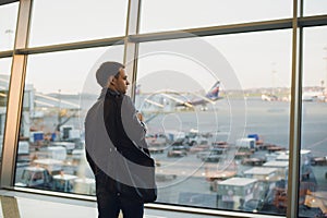 Travel concept with young man in airport interior with city view and a plane flying by.