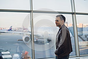 Travel concept with young man in airport interior with city view and a plane flying by.