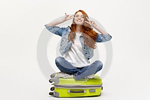 Travel concept: young smiling caucasian woman siting on suitcase showing two fingers. over white background.
