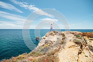 Travel concept. Young tourist man standing on the edge of reef enjoying ocean or sea view of turquoise water with raised hands