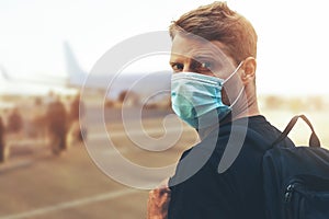 Travel during coronavirus pandemic - young man wearing protective face mask and boarding plane at airport