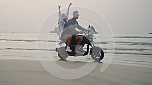 Travel couple ride motorcycle along sea beach on sunrise. Intraframe installation from bike wheels reflection, trace to