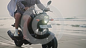 Travel couple ride motorcycle along sea beach on sunrise. Intraframe installation from people to wheels . Tourists drive