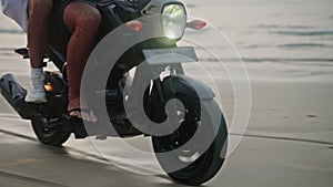 Travel couple ride motorcycle along sea beach on sunrise. Intraframe installation from people to wheels . Tourists drive