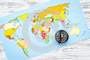 Travel direction and trip planning concept with compass and map of the world on gray wooden background top view