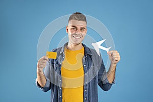 Travel expenses and trip budget concept. Handsome millennial guy with credit card and paper plane on blue background
