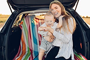 Travel - family ready to go on summer vacation, Happy mom with a small child in the trunk of a car