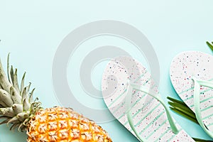 Travel flat lay items: fresh pineapple, beach slippers  and palm leaf lying on blue background. Place for text. Top view. Summer