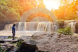 Travel and freedom. Young Asian man  with hand up enjoying tropical waterfall view. Waterfall in the rain forest. Man standing in