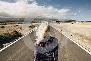 Travel and future choiches concept with blonde young millennial girl viewed from rear walking on a straight long road - airplane