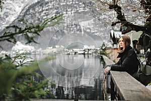 Travel girl with a backpack enjoying the magnificent snowy mountain in village of Hallstatt with Lake Hallstadt in winter. Travel