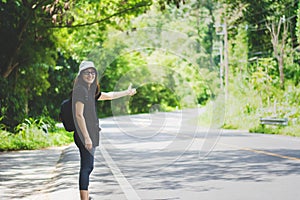 Hitchhiker woman with hat and backpack walking on a road