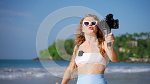 Travel influencer films beach vlog with pro camera, wireless lav mic. Female blogger seaside scenery, records tips for