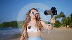 Travel influencer records beach vlog with pro camera, wireless lav mic. Female blogger captures scenic coast, shares