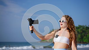 Travel influencer records beach vlog with pro camera, wireless lav mic. Sunlit tropical backdrop, engaging viewers, solo