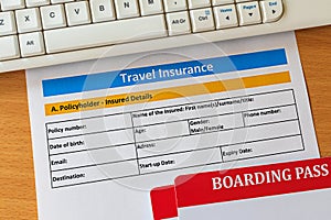 Travel insurance form on wooden table with boarding pass ticket and keyboard.