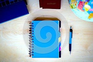 Travel items, blue notepad, pen, pc, globe on wooden background